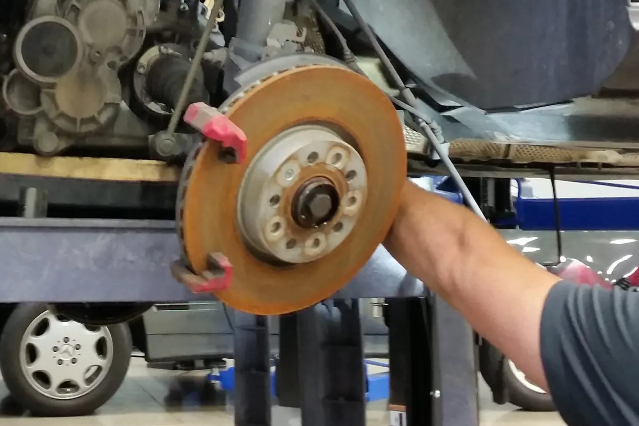 Technician removing a worn brake rotor, with the wheel hub and ABS ring exposed