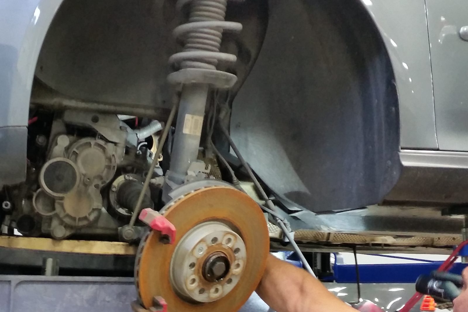 Front strut and coil spring on a vehicle raised on a lift, brake rotor and CV axle visible
