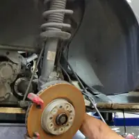 Front strut and coil spring on a vehicle raised on a lift, brake rotor and CV axle visible